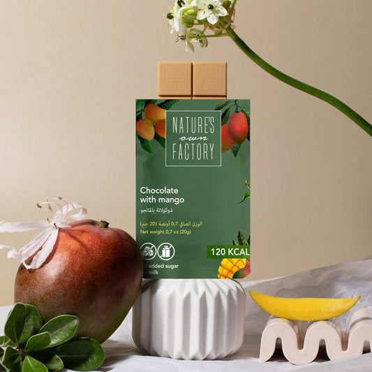 Elegant display of Nature’s Own Factory chocolate with mango, surrounded by fresh mango, flowers, and white decorative elements on a beige background