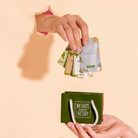 Hand placing mini products into a green 'Nature's own Factory' mini chocolate set bag on a beige background