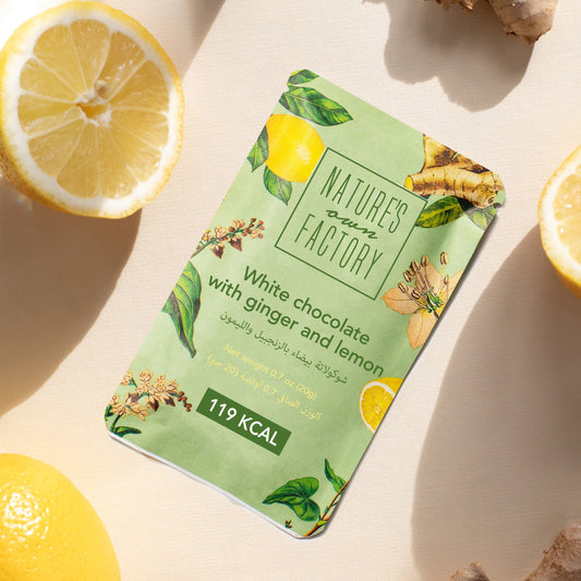 Nature’s Own Factory white chocolate with ginger and lemon bar surrounded by fresh lemons and ginger on a beige background