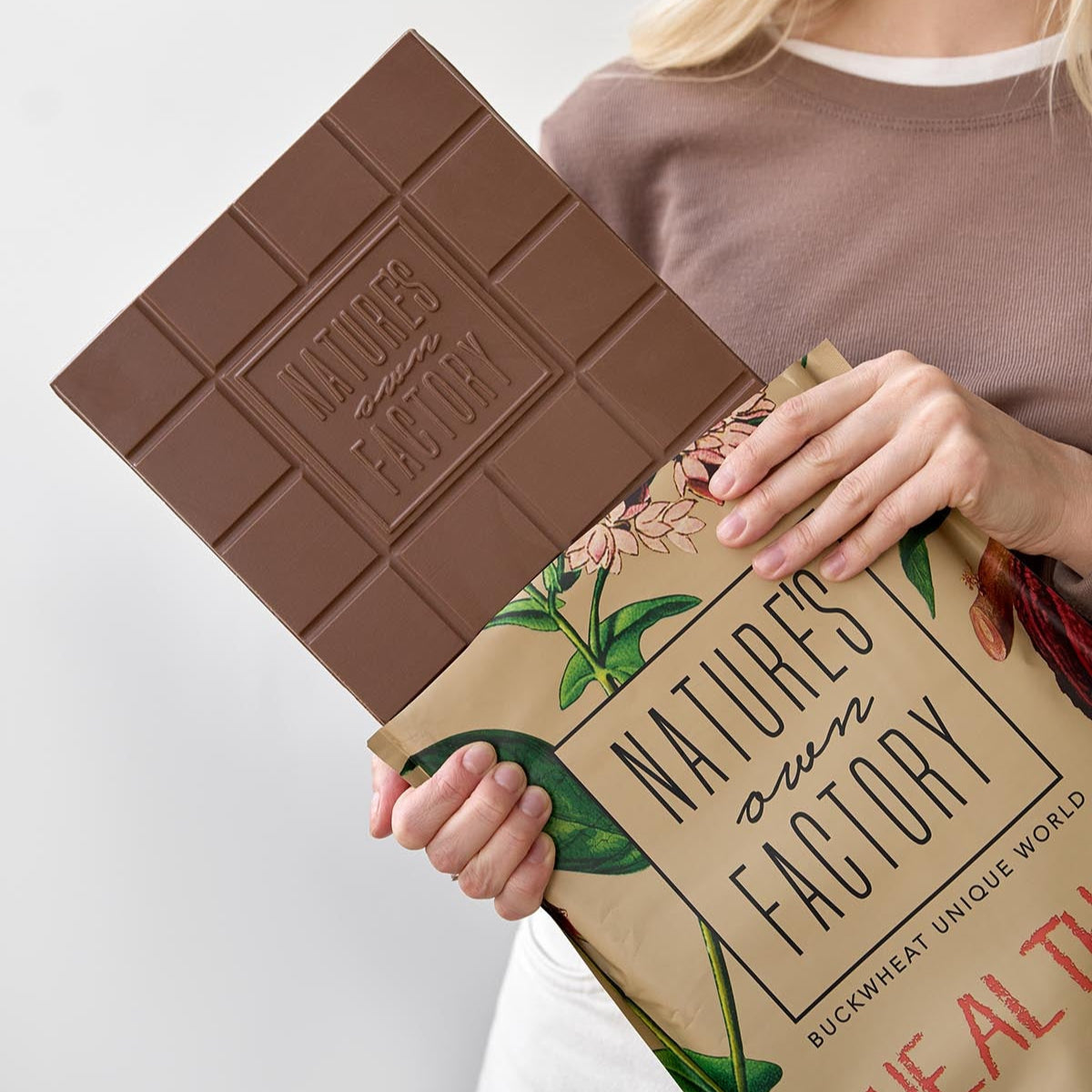 Person holding the milk chocolate bar 2kg and its packaging with the 'Nature's Own Factory' branding.