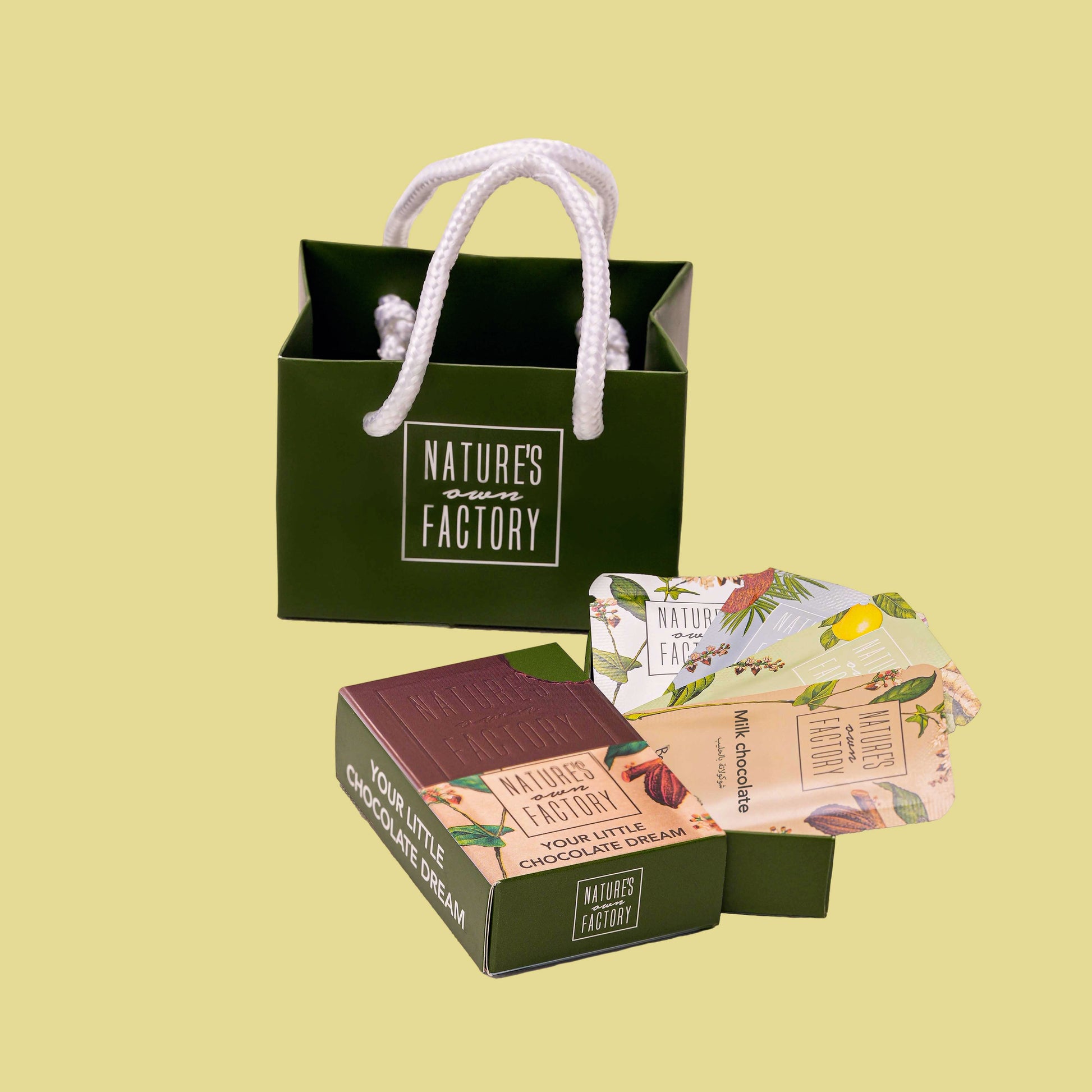 Green gift bag with 'Nature's Own Factory' Mini chocolate set on a light yellow background